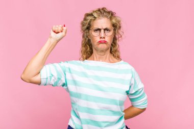 Orta yaşlı kadın ciddi, güçlü ve isyankar hissediyor, yumruğunu kaldırıyor, protesto ediyor ya da devrim için savaşıyor.