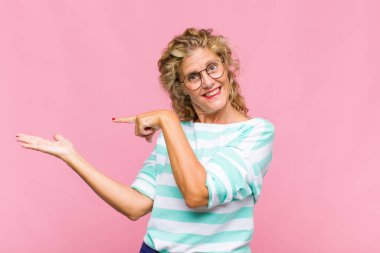 Orta yaşlı kadın neşeyle gülümsüyor ve yan taraftaki fotokopi alanına işaret ediyor, bir nesneyi gösteriyor veya reklamını yapıyor.