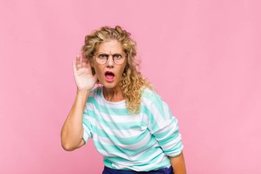 Orta yaşlı bir kadın ciddi ve meraklı görünüyor, dinliyor, gizli bir konuşma veya dedikodu duymaya çalışıyor, kulak misafiri oluyor.