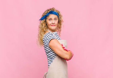 Kollarını kavuşturup kameraya gülümseyen orta yaşlı bir kadın ve mutlu, kendinden emin, tatmin olmuş bir ifade.