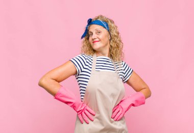 Orta yaşlı bir kadın mutlu, neşeli ve kendinden emin görünüyor, gururla gülümsüyor ve iki elini de kalça temizleyicisi kavramında kullanıyor.