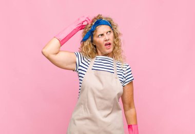 Orta yaşlı kadın şaşkın ve kafası karışmış hissediyor. Kafasını kaşıyor ve temizlikçi konseptine bakıyor.