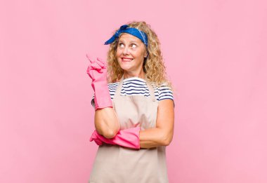 Orta yaşlı bir kadın mutlu bir şekilde gülümsüyor ve yan bakıyor, merak ediyor, düşünüyor ya da bir fikir bekçisi kavramına sahip.