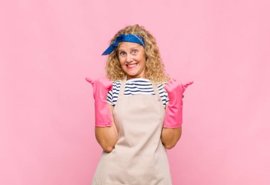 Orta yaşlı bir kadın neşeyle gülümsüyor ve mutlu görünüyor, kaygısız ve pozitif hissediyor iki baş parmağıyla hizmetçi kavramını destekliyor.