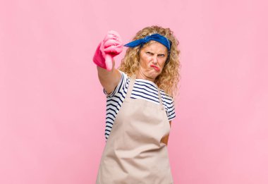 Orta yaşlı bir kadın sinirli, sinirli, hayal kırıklığına uğramış ya da hayal kırıklığına uğramış, ciddi bir hizmetçi konseptiyle baş parmaklarını göstermiyor.