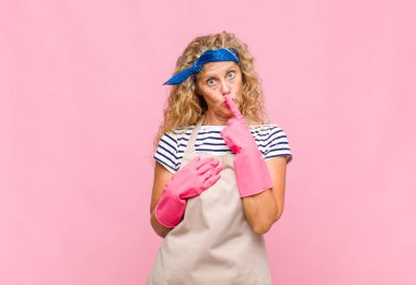 Orta yaşlı kadın ciddi görünüyor ve parmaklarını dudaklarına bastırıp sessizlik ya da sessizlik talep ediyor, gizli bir hizmetçi konseptini koruyor.