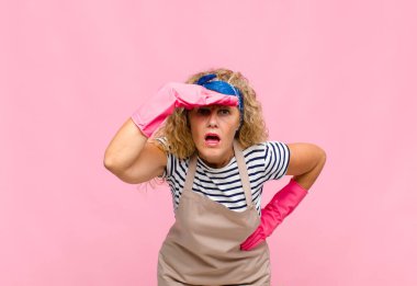 Orta yaşlı kadın şaşkın ve şaşkın görünüyor, alnının üstünden uzaklara bakıyor, kahya konseptini izliyor ya da arıyor.