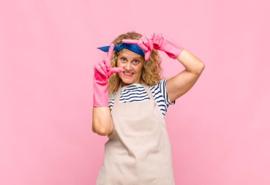 Orta yaşlı bir kadın mutlu, arkadaş canlısı ve pozitif hissediyor, gülümsüyor ve elleri hizmetçi konseptiyle bir portre veya fotoğraf çerçevesi yapıyor.