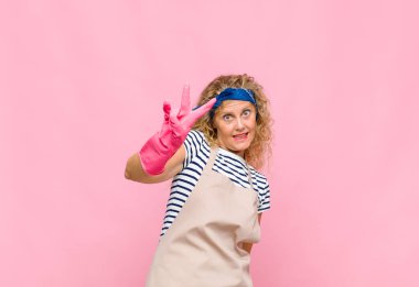 Orta yaşlı bir kadın gülümsüyor ve arkadaş canlısı görünüyor. İki ya da iki numarayı gösteriyor. Elleri önde, temizlikçi konseptini sayıyor.