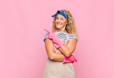 Orta yaşlı kadın neşeyle gülümsüyor, mutlu hissediyor ve yan ve yukarı doğru işaret ediyor, fotokopi uzayı temizleyicisi konseptinde nesne gösteriyor.