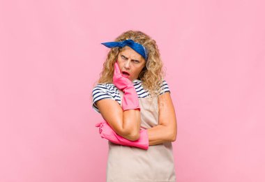 Orta yaşlı bir kadın şok ve inanmazlık içinde, elleri yanakları ve kolları çaprazlanmış, sersemlemiş ve hayrete düşmüş bir ev hanımı gibi hissediyor.