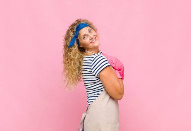 Orta yaşlı bir kadın neşeli bir şekilde gülümsüyor, mutlu, tatmin olmuş ve rahatlamış hissediyor, kollarını kavuşturup, hizmetçi konseptine bakıyor.