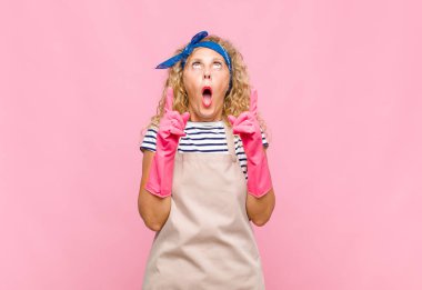 Orta yaşlı kadın şaşırmış, şaşırmış ve ağzı açık bir şekilde iki eliyle uzayın temizlikçisi konseptini taklit ediyor.