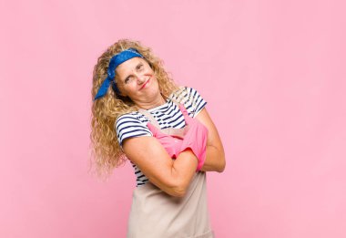 Orta yaşlı bir kadın kollarını kavuşturup mutlu bir şekilde gülüyor, rahat, pozitif ve tatmin edici bir poz veriyor.