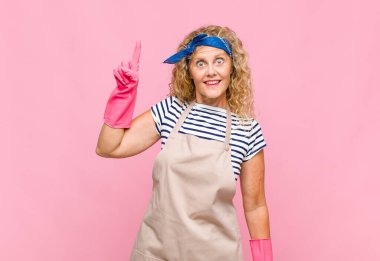 Orta yaşlı kadın neşeli ve mutlu bir şekilde gülümsüyor, tek eliyle uzay hizmetçisi konseptini taklit ediyor.