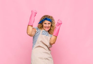 Orta yaşlı bir kadın muzaffer bir şekilde bağırıyor. Heyecanlı, mutlu ve şaşırmış görünüyor. Hizmetçi konseptini kutluyor.