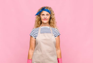 Orta yaşlı bir kadın pozitif ve kendinden emin gülümsüyor. Tatmin olmuş, arkadaş canlısı ve mutlu bir hizmetçi gibi görünüyor.