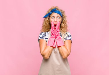 Orta yaşlı kadın şok olmuş ve korkmuş hissediyor, ağzı açık ve elleri yanaklarında, hizmetçi konseptiyle korkmuş görünüyor.