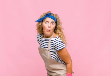 Aptal, çılgın, şaşırmış bir ifadeyle orta yaşlı bir kadın, yanakları şişmiş, doldurulmuş, şişman ve yemek hizmetçisi konseptiyle dolu.