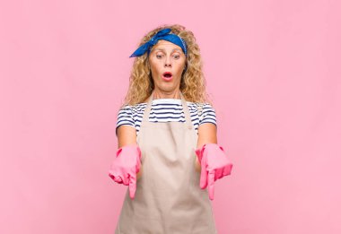 Orta yaşlı, ağzı açık bir kadın iki eliyle aşağıya doğru bakıyor. Şaşırmış, şaşırmış ve şaşırmış görünüyor.