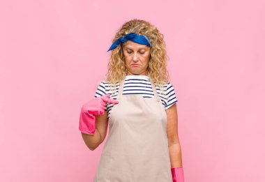 Orta yaşlı bir kadın neşeli ve sıradan bir şekilde gülümsüyor, aşağıya bakıyor ve göğüs temizleyicisi kavramına işaret ediyor.