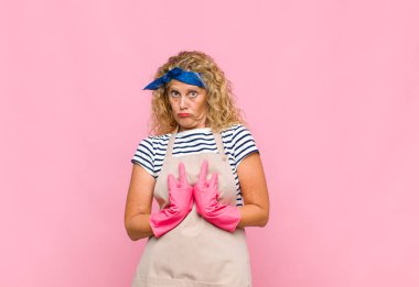 Orta yaşlı bir kadın, şaşkın ve tuhaf bakışlarıyla kendini işaret ediyor. Seçilmiş hizmetçi konseptine şaşırmış ve şaşırmış.