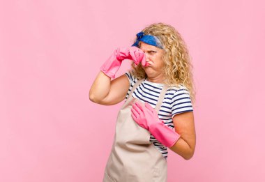 Orta yaşlı bir kadın iğreniyor, pis ve nahoş kokulu hizmetçi konseptini koklamamak için burnunu tutuyor.