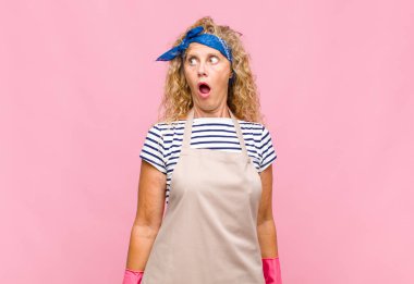 Orta yaşlı bir kadın şaşkın, mutlu, şaşkın ve şaşırmış hissediyor, ağzı açık hizmetçi konseptiyle yan tarafa bakıyor.