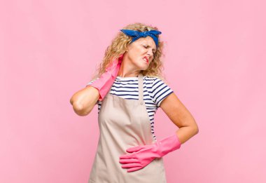 Orta yaşlı bir kadın stresli, hayal kırıklığına uğramış ve yorgun hissediyor. Endişeli, sorunlu görünümlü bir hizmetçi konseptiyle boynunu okşuyor.