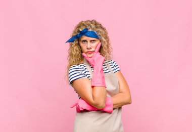 Orta yaşlı bir kadın ciddi, düşünceli ve güvensiz görünüyor, bir kolu çapraz ve çene üzerinde, seçenekleri tartan hizmetçi konsepti