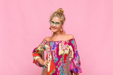 Orta yaşlı bir kadın mutlu bir şekilde gülümsüyor. Kendine güvenen, olumlu, gururlu ve arkadaş canlısı bir tavırla.