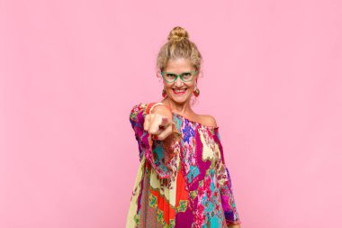 Orta yaşlı bir kadın kameraya bakıyor, kendinden emin, arkadaş canlısı bir gülümsemeyle, seni seçiyor.