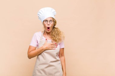 Orta yaşlı bir fırıncı şaşkın ve şaşırmış hissediyor, gülümsüyor, el ele tutuşuyor, tek olmaktan ya da minnettarlık göstermekten mutlu.