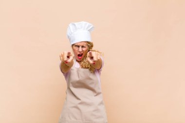 Orta yaşlı bir fırıncı, kameraya iki parmağıyla ve kızgın bir ifadeyle bakarak sana görevini yapmanı söylüyor.