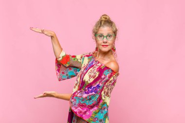 Orta yaşlı bir kadın bir objeyi iki eliyle fotokopi alanında tutuyor, bir objeyi gösteriyor, sunuyor ya da reklamını yapıyor.