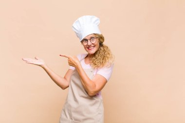 Orta yaşlı fırıncı neşeli bir şekilde gülümseyen ve yan taraftaki fotokopi alanına işaret eden, bir nesneyi gösteren ya da reklamını yapan