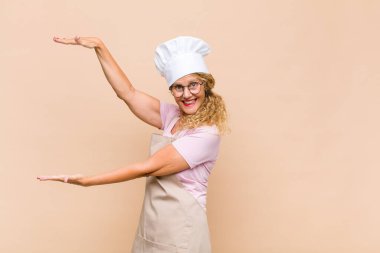 Orta yaşlı fırıncı gülümsüyor, mutlu, pozitif ve tatmin olmuş hissediyor, fotokopi alanında nesne veya konsept tutuyor veya gösteriyor