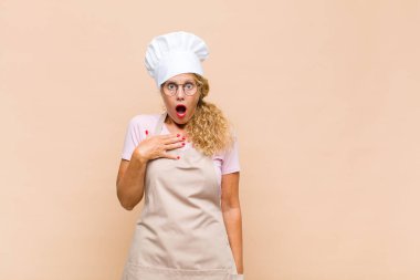 Orta yaşlı kadın fırıncı şaşkın, şaşkın ve şaşırmış hissediyor, elleri göğsünde ve ağzı açık, kim olduğumu söylüyor, ben?