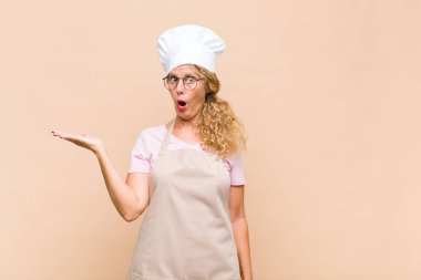 Orta yaşlı fırıncı şaşırmış ve şoka uğramış görünüyor. Çenesi düşmüş ve eli açık bir objeyi tutuyor.