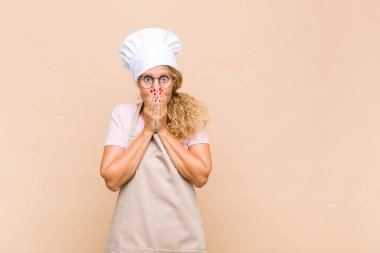 Orta yaşlı kadın fırıncı mutlu ve heyecanlı, şaşırmış ve şaşırmış ağızları ellerle kaplayan, tatlı bir ifadeyle kıkırdayan