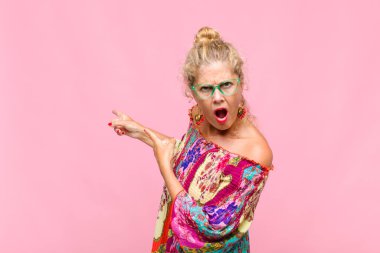 Orta yaşlı kadın şaşkın ve şaşırmış hissediyor. Kenardaki fotokopi alanını işaret ediyor. Şaşırmış ve ağzı açık bakıyor.