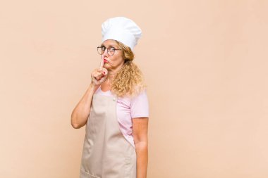 Orta yaşlı bir fırıncı sessizlik ve sessizlik istiyor, parmağıyla ağzının önünde işaret ediyor, 