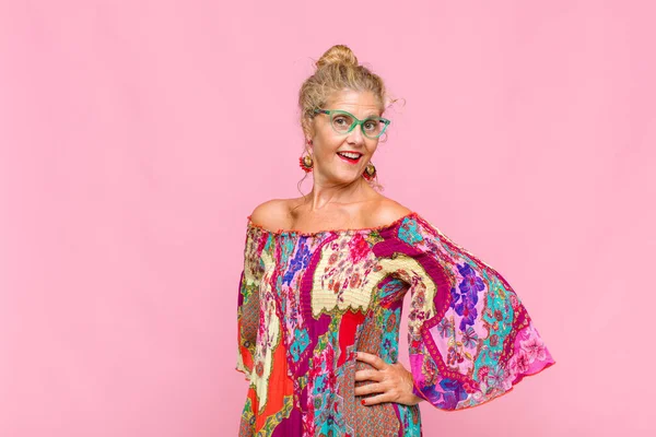 Orta yaşlı bir kadın mutlu, neşeli ve kendinden emin görünüyor. Gururla gülümsüyor ve iki elini de kalçasında istiyor.