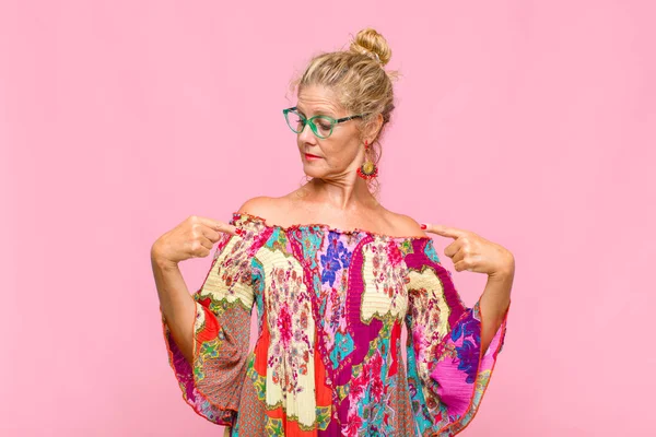 Orta yaşlı kadın gururlu, pozitif ve rahat görünüyor. İki eliyle göğsünü gösteriyor.