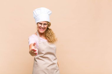 Orta yaşlı fırıncı gülümsüyor, mutlu, kendinden emin ve arkadaş canlısı görünüyor, bir anlaşma yapmak için el sıkışma teklif ediyor, işbirliği yapıyor.