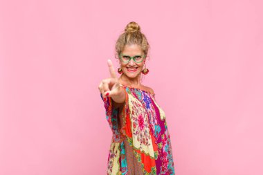 Orta yaşlı bir kadın gururla gülümsüyor ve gururla bir numaralı pozunu veriyor, kendini lider gibi hissediyor.