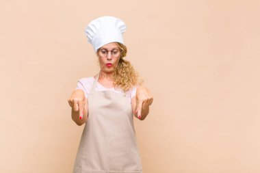 Orta yaşlı fırıncı, ağzı açık, iki eliyle aşağıya bakıyor, şaşkın, şaşkın ve şaşırmış görünüyor.