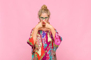 Orta yaşlı bir kadın ciddi ve hoşnutsuz görünüyor. Her iki eli de önde, reddedilmek üzere, sessizlik istiyor.