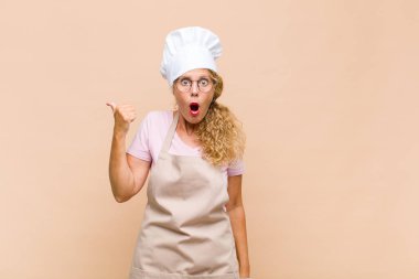 Orta yaşlı fırıncı kadın inanamadığı için hayrete düşmüş, yan taraftaki objeyi işaret ederek 