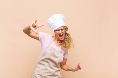 Orta yaşlı bir fırıncı kendini mutlu, eğlenceli, kendinden emin, pozitif ve asi hisseder, elle kaya ya da ağır metal işareti yapar.